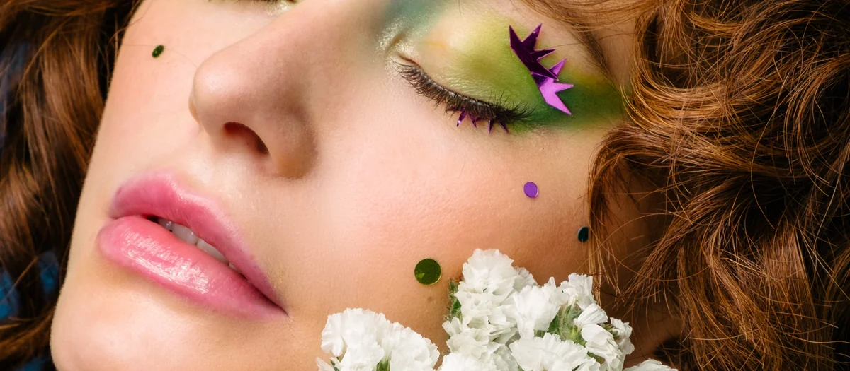 Beauty close-up with green eye makeup and orange gerbera flowers