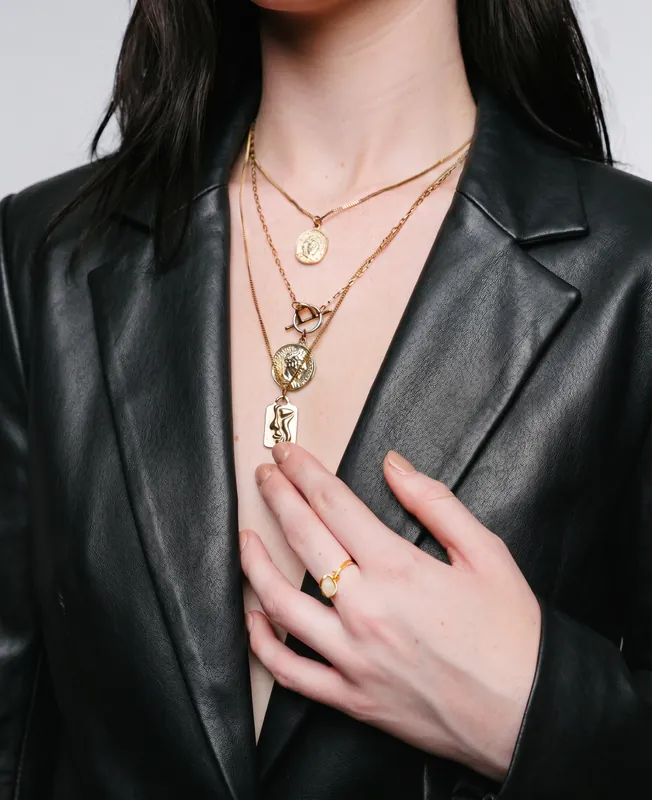 Layered gold pendant necklaces over a black leather blazer, an example of Vidd Studios jewelry work