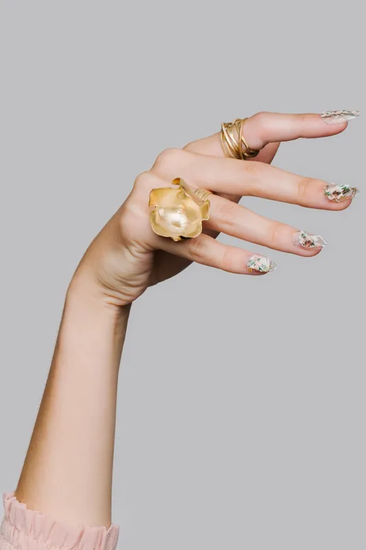 Hand wearing a sculptural gold statement ring on a grey background, an example of Vidd Studios jewelry work