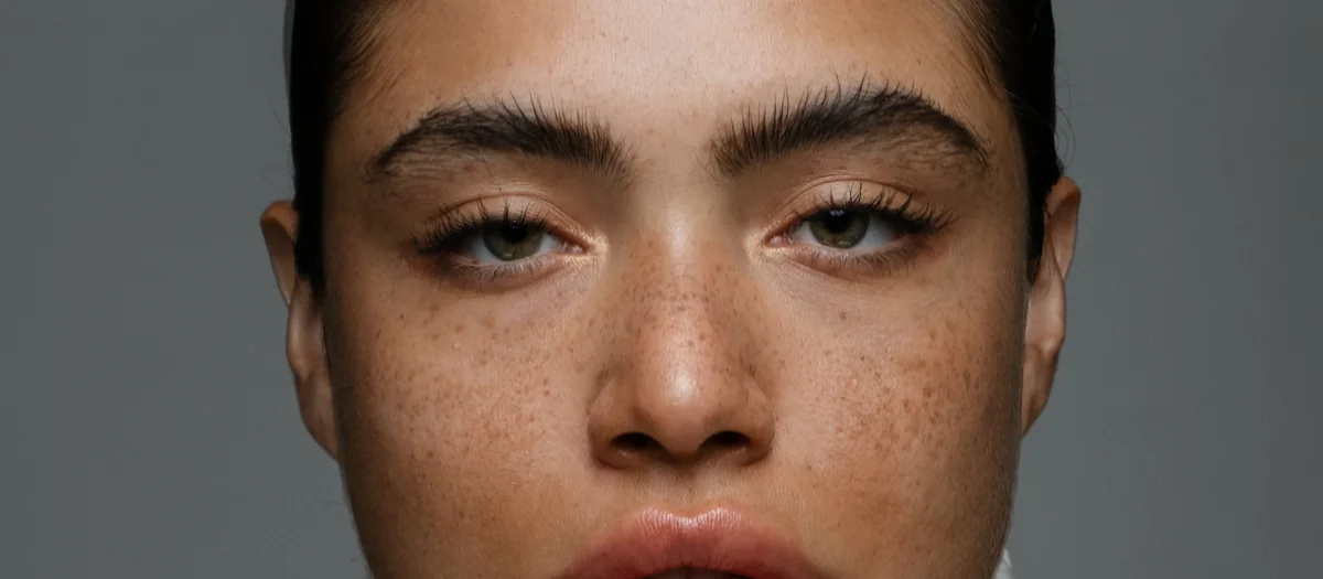 Retouched beauty portrait of a woman with freckles in a white turtleneck on a gray backdrop
